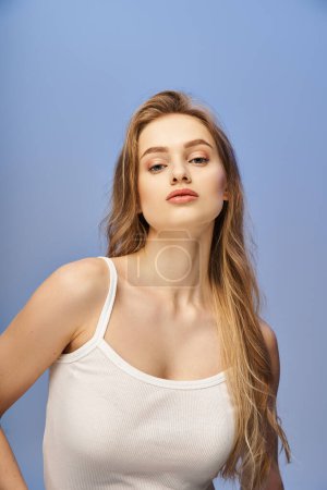 Une jeune femme blonde respire l'élégance tout en posant dans un débardeur blanc dans un décor de studio.