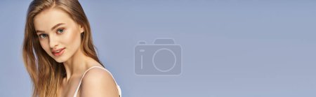 Téléchargez les photos : Une jeune femme aux longs cheveux blonds se tient gracieusement devant un ciel bleu vibrant. - en image libre de droit