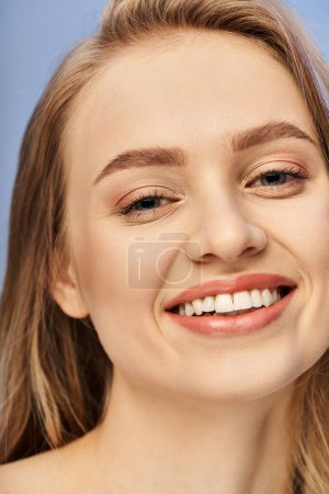 Młoda blondynka uśmiecha się radośnie pokazując białe zęby w studio.