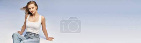 Téléchargez les photos : Une jeune femme blonde pose élégamment dans une chemise blanche et un jean dans un décor studio, exsudant une beauté rayonnante et éthérée. - en image libre de droit