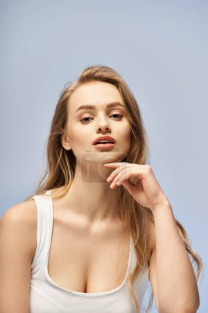 Téléchargez les photos : Une jeune femme blonde respire l'élégance dans un haut blanc alors qu'elle pose gracieusement pour la caméra dans un décor de studio. - en image libre de droit