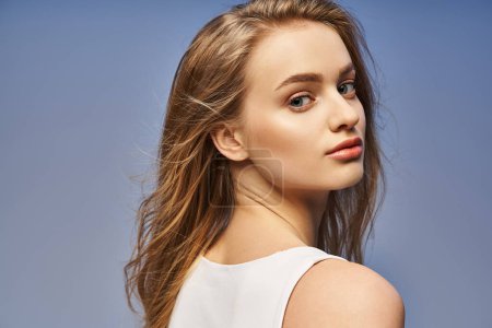 A young, blonde woman exudes grace in a white top, showcasing her flowing long hair in a studio setting.