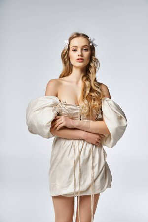 A young, blonde woman exudes elegance in a white dress, striking a pose for a portrait in a studio setting.