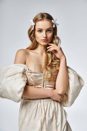A young, blonde woman wearing a white dress strikes a pose in a stylish studio setting.