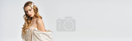 Eine junge, blonde Frau strahlt Anmut und Eleganz aus, während sie in einem weißen Kleid für ein Porträt im Studio posiert.