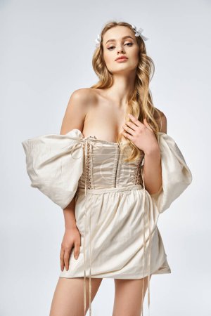 Eine atemberaubende junge blonde Frau posiert elegant in einem fließenden weißen Kleid in einem Studio-Setting.