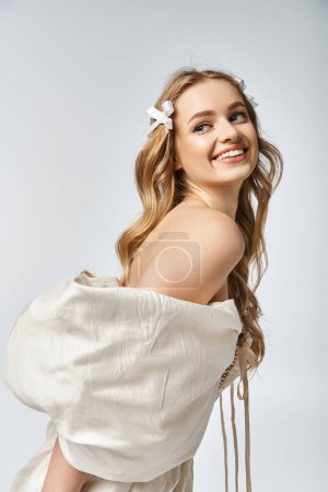 Téléchargez les photos : Une jeune femme blonde pose gracieusement en robe blanche dans un décor de studio. - en image libre de droit
