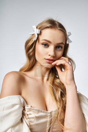 A young, blonde woman exudes tranquility with a white bow gracefully adorning her hair in a studio setting.