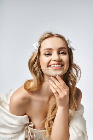 Eine auffallend schöne junge blonde Frau posiert selbstbewusst in einem Studio-Setting und strahlt in ihrem weißen Kleid Eleganz aus.