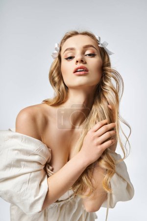 Téléchargez les photos : Une jeune femme aux longs cheveux blonds pose dans une robe blanche fluide dans un décor de studio, respirant élégance et grâce. - en image libre de droit