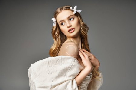 A young, blonde woman radiates grace in a white dress with a bow in her hair, exuding timeless elegance in a studio setting.