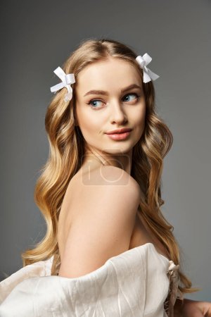 Téléchargez les photos : Une jeune femme blonde aux cheveux longs pose élégamment dans une robe blanche fluide dans un décor de studio. - en image libre de droit