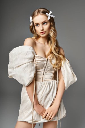 A young, blonde woman stands in a studio wearing a short dress and a bow in her hair, exuding a sense of elegance and sweetness.