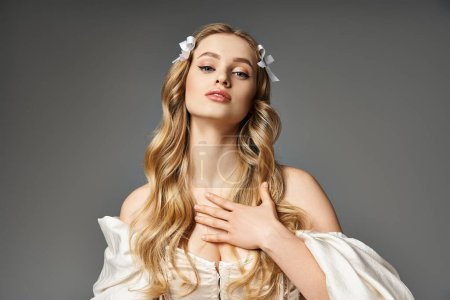 A young woman with long blonde hair, dressed in a flowing white gown, exudes a sense of ethereal beauty in a studio setting.