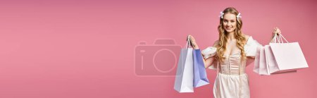 Photo for A young, blonde woman in a white dress holding colorful shopping bags against a plain backdrop. - Royalty Free Image