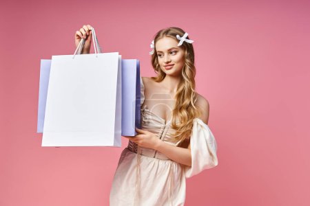 A stunning young blonde woman gracefully holds a shopping bag in a studio setting.