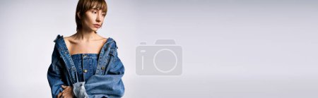 Eine junge Frau mit kurzen Haaren posiert selbstbewusst für ein Foto in einem schicken Jeanskleid in einem Studio-Setting.
