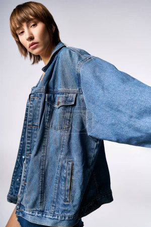 Téléchargez les photos : Une jeune femme aux cheveux courts pose en toute confiance pour une photo en studio, vêtue d'une veste en jean tendance. - en image libre de droit