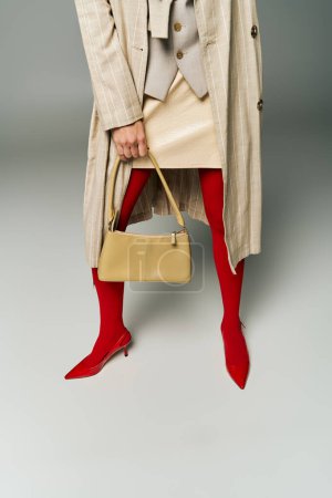 Eine modische junge Frau steht selbstbewusst im Trenchcoat und hält eine stylische Handtasche in der Hand.