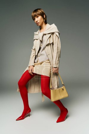 Eine stylische junge Frau in leuchtend roten Strumpfhosen und schickem Trenchcoat posiert selbstbewusst in einem Studio-Setting.