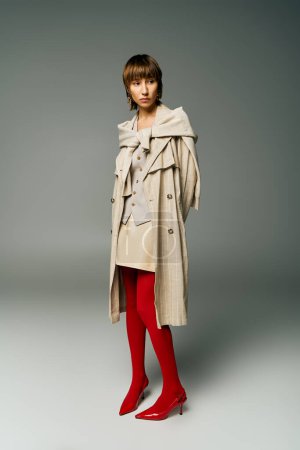 A stylish young woman with short hair poses confidently in a trench coat and vibrant red tights, exuding a sense of sophistication.