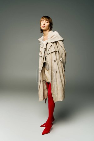A young woman exudes elegance in a trench coat and vibrant red tights, striking a pose in a studio setting.