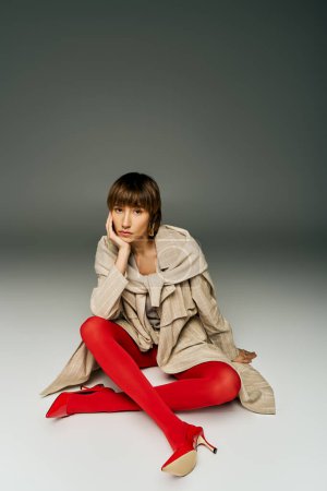 Eine junge Frau mit kurzen Haaren sitzt anmutig auf dem Boden, gekleidet in leuchtend rote Strumpfhosen in einem Studio-Setting.