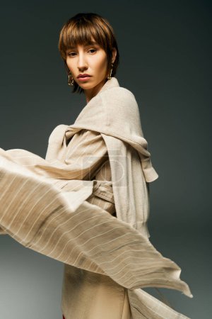 A young woman with short hair, wearing a flowing dress and a scarf, exudes elegance and grace in a studio setting.