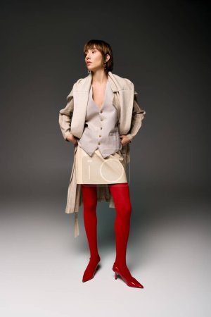A young woman with short hair strikes a pose in tights and a coat in a studio setting.