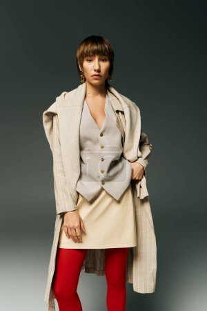 A stylish young woman with short hair poses in tights and a coat in a studio setting, exuding confidence and elegance.
