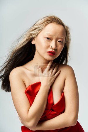 Vibrant Asian woman exudes elegance in a lively pose in a red dress.