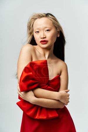 A captivating Asian woman in a striking red dress with arms confidently crossed.