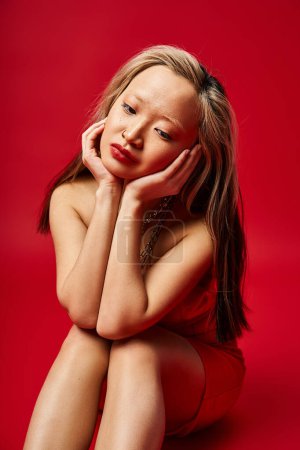 Téléchargez les photos : Femme asiatique vibrante en vêtements colorés assis, mains sur le visage. - en image libre de droit