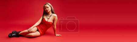 Foto de An attractive Asian woman in a vibrant red dress gracefully sitting on the floor. - Imagen libre de derechos