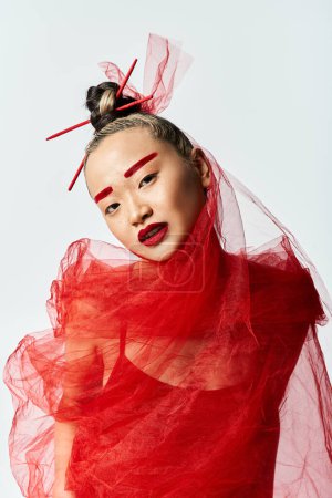 Foto de Una atractiva mujer asiática en un vestido rojo golpea una pose poderosa con un velo en la cabeza. - Imagen libre de derechos