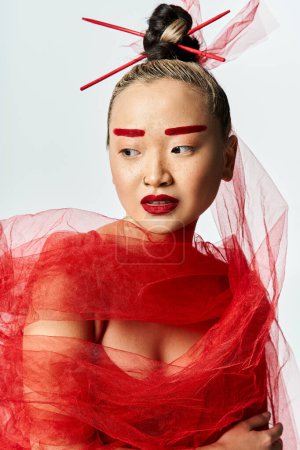 Asian woman in red makeup and a head veil striking a pose.