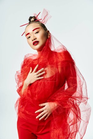 An attractive Asian woman in vibrant red attire dances gracefully with a veil on her head.