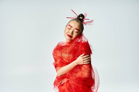 A vibrant Asian woman in a red dress is wrapped in veil.