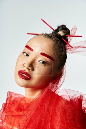 Femme asiatique en robe rouge pose avec des bâtons qui sortent de son visage.