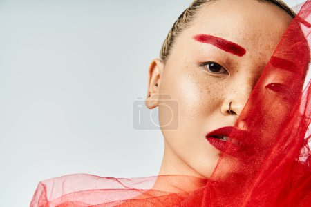 Eine Asiatin mit auffallend rotem Make-up und fließendem roten Schleier posiert elegant.