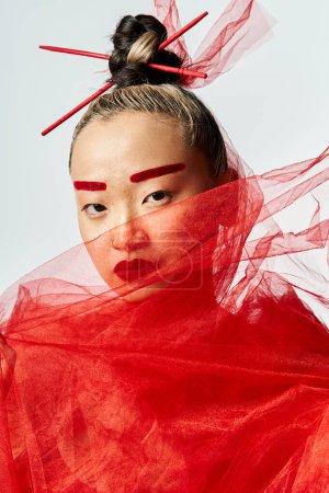 Asian woman striking pose in red dress with flowing veil.