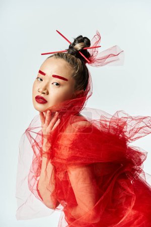 Asian woman in red dress and veil posing gracefully.