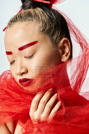 Téléchargez les photos : Femme asiatique avec un maquillage rouge audacieux et un voile de tête posant élégamment. - en image libre de droit