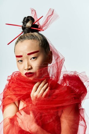 Femme asiatique en robe rouge avec voile pose élégamment.
