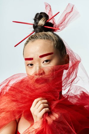 An attractive Asian woman in a vibrant red dress poses with a delicate veil on her head.