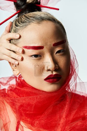 Mujer asiática con maquillaje rojo y un velo, golpeando una pose.
