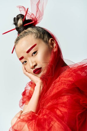 Foto de Una cautivadora asiática vestida de rojo y maquillada alcanza una pose dinámica. - Imagen libre de derechos
