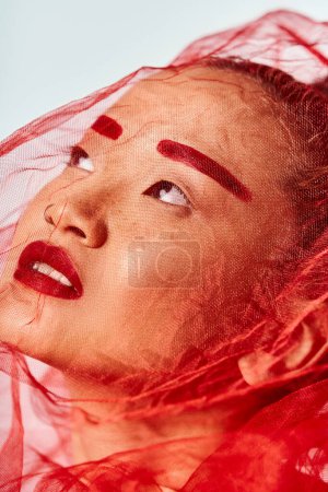 Foto de Una mujer asiática adornada con vibrante maquillaje rojo y un velo posa activamente. - Imagen libre de derechos