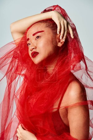 Asian woman in red dress striking a pose with a delicate veil on her head.