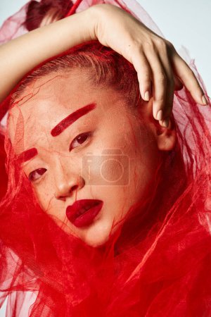 Foto de Mujer asiática en vestido rojo, manos en la cabeza, pose llamativa. - Imagen libre de derechos
